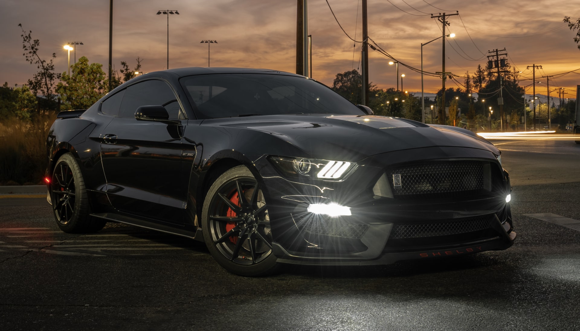 black mustang with headlights on at sunset
