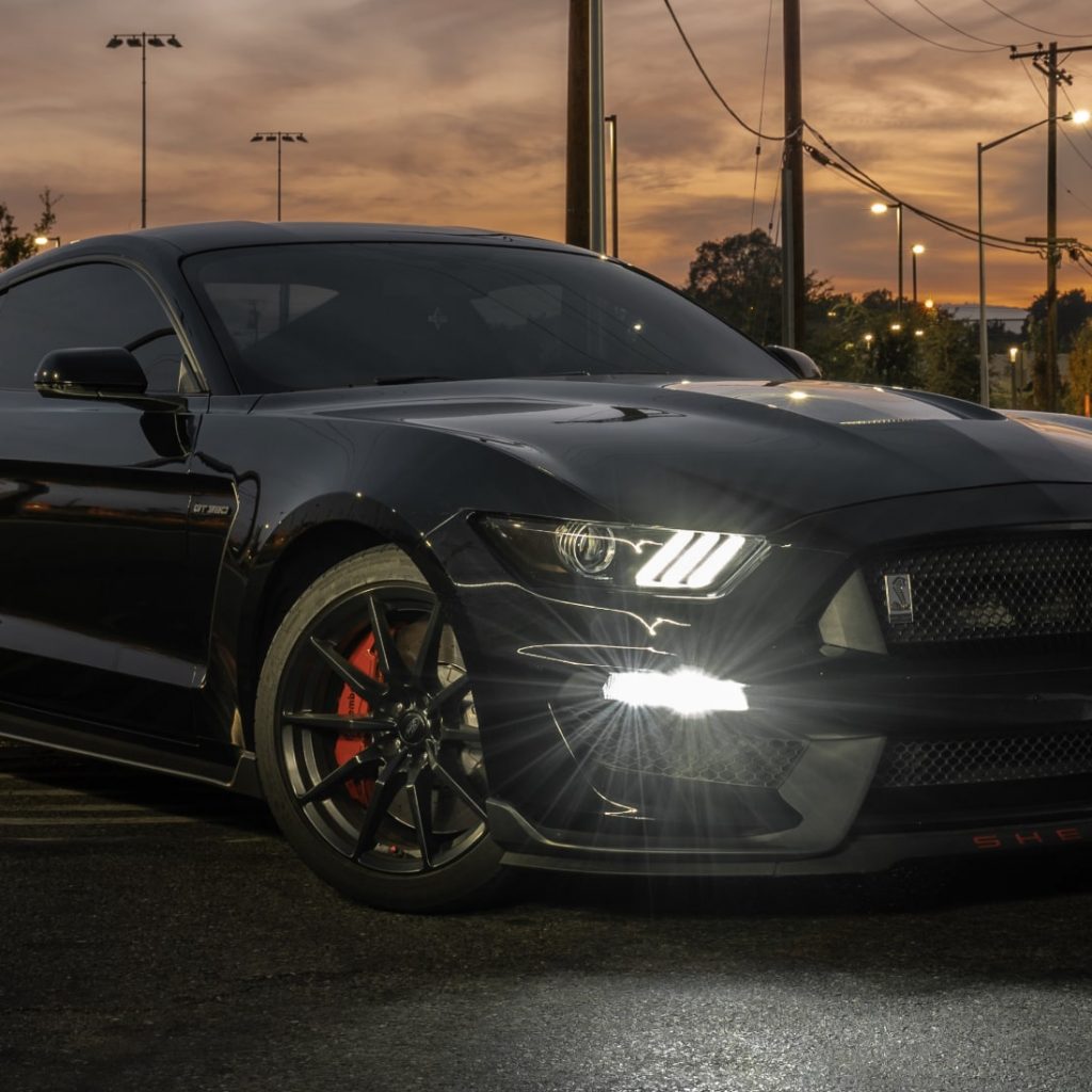 black mustang with headlights on at sunset